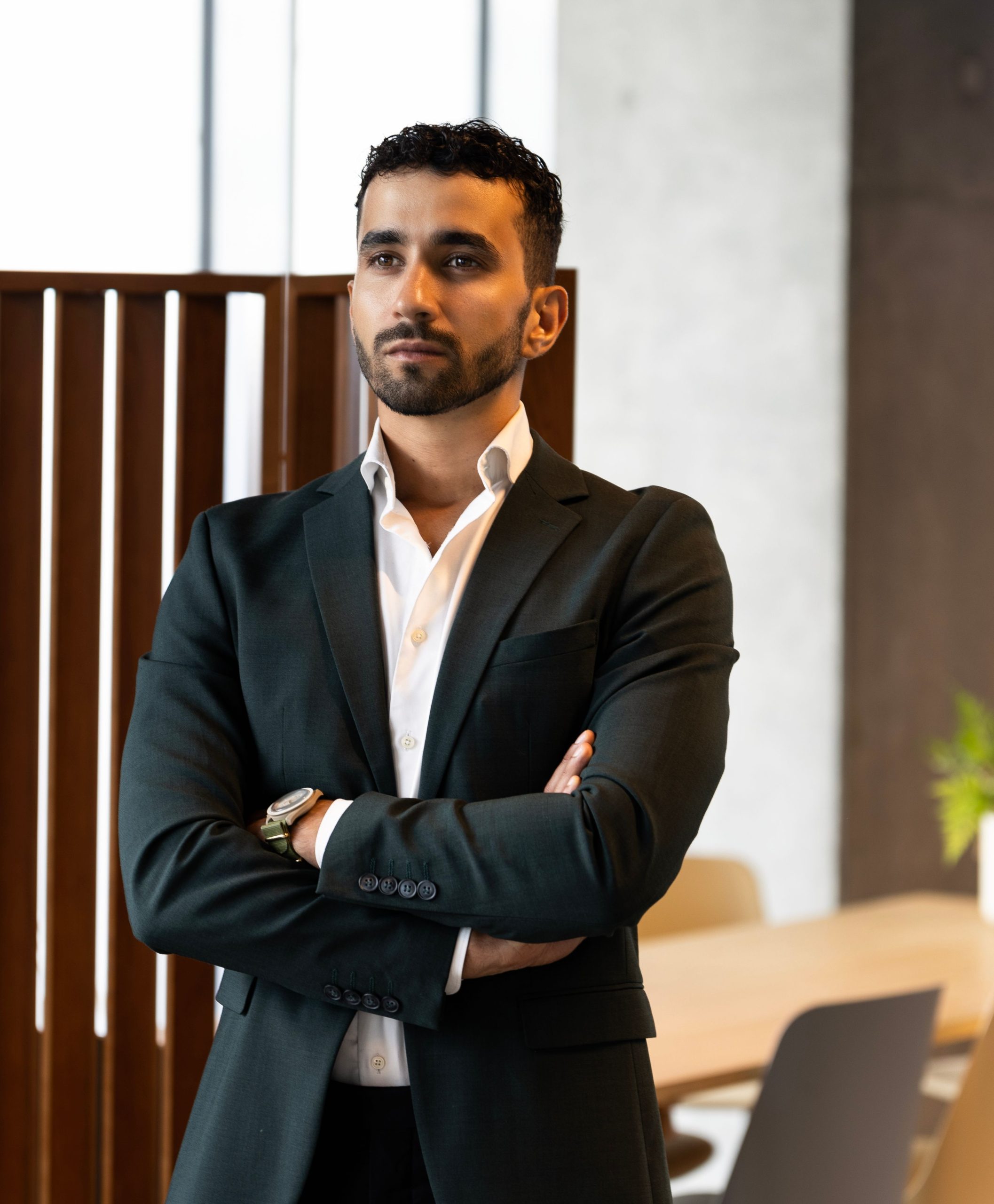 A confident businessman in a suit standing in a modern office with natural lighting.